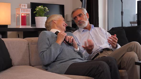 Elderly Couple Sits in A Living Room and Watches TV and Playfully Fights Over the Remote Control