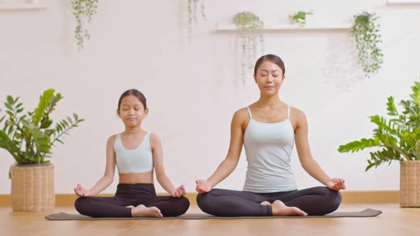 Healthy couple mom and little girl doing yoga exercise on yoga mat at home.Female mother and daughte