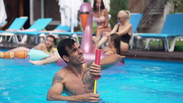 Portrait of Carefree Joyful Middle Eastern Adult Man Playing with Water Gun in Swimming Pool
