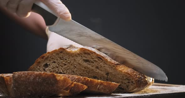 Person Cuts Slices of Hot Rye Bread Loaf on Wooden Board