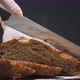 Person Cuts Slices of Hot Rye Bread Loaf on Wooden Board - VideoHive Item for Sale