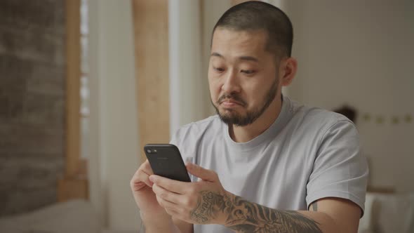 Young Adult Asian Man is Online Shopping on His Smart Phone