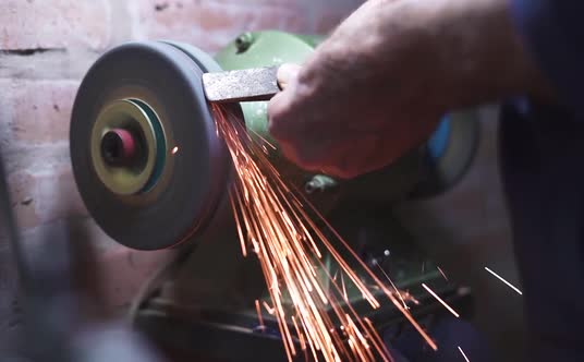 Worker Man Making Sparks While Grinds Metal With The Bench Grinder