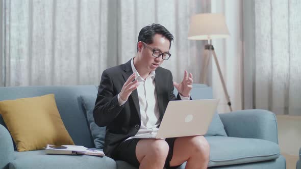 Asian Businessman In Jacket And Shorts Having Video Call On A Laptop At Home