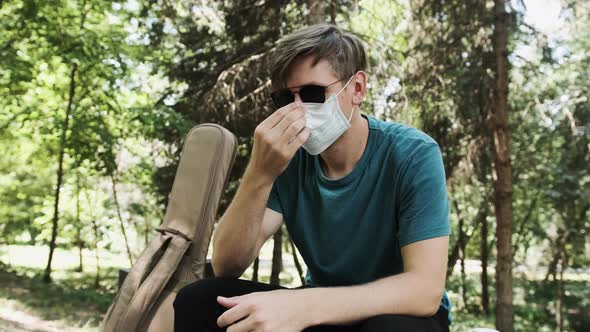 Young Man Putting on Face a Medical Mask While Is Sitting in the Park
