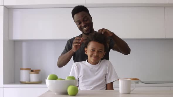 African American Father Doing Head Massage for His Son at Table in Apartment Room Spbi