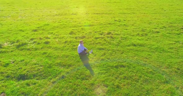 Low Orbital Flight Around Man on Green Grass with Notebook Pad at Yellow Rural Field.