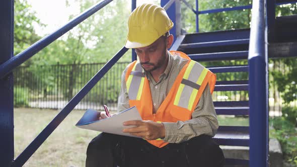 Civil Engineer in Helmet and Safety Vest Taking Notes in Notepad