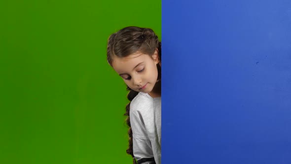 Child Looks Out From Behind the Blue Board and Laughs. Green Screen