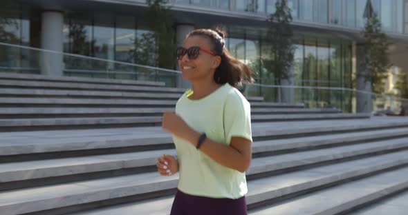 Side View of Sporty Young Mixedrace Woman Running on Sidewalk in Morning