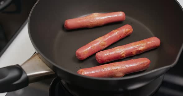 Cooking sausages on the fry pan in kitchen for breakfast