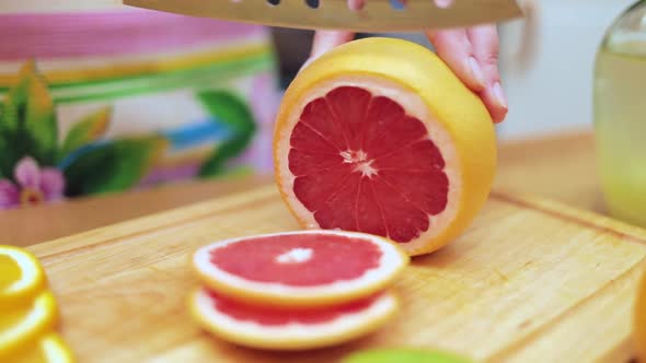 Women's Hands Housewives Cut with a Knife Fresh Grapefruit on the Cutting Board of the Kitchen Table