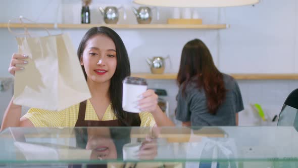 Attractive asian female cafe worker  giving takeaway food bag to customer.