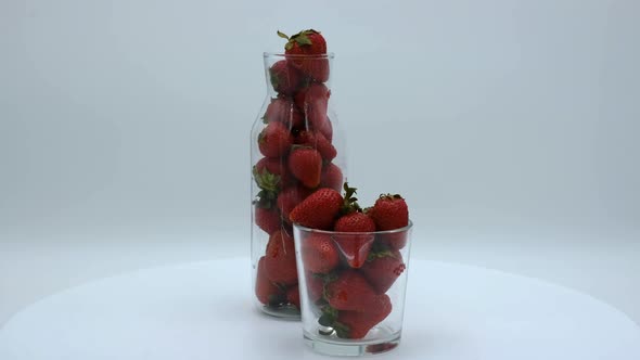 Strawberries in a clear bottle and glass rotating on a white background. Strawberry ripe season