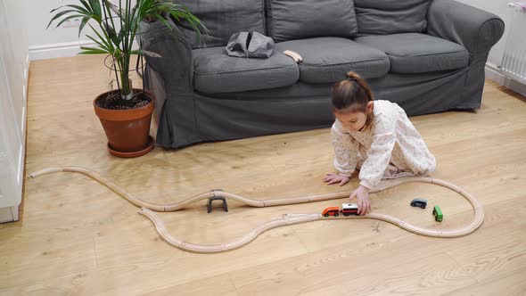 Toddler Girl in White Dress Plays with Wooden Train at Home in the Living Room