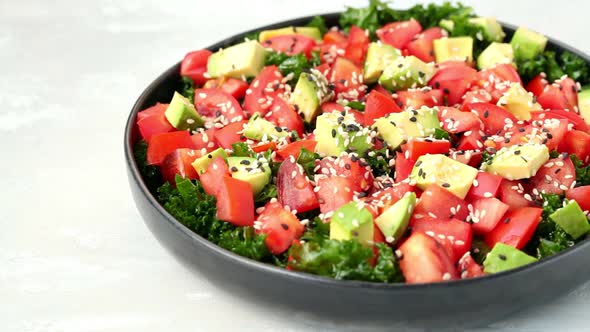 Kale salad with tomatoes and avocado in black plate. 