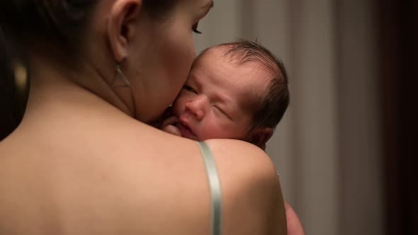 Young mother holds her newborn son on her shoulder