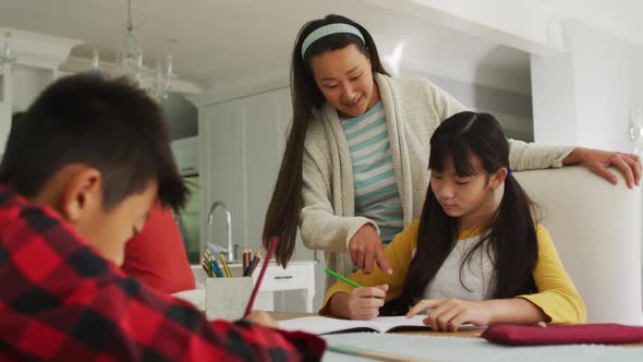 Asian mother in kitchen helping son and daughter doing schoolwork