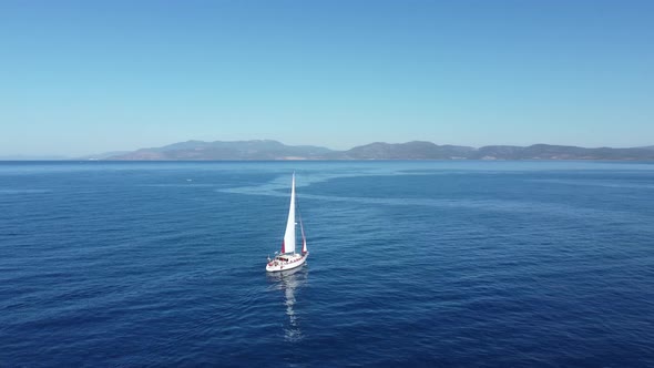 Aerial view of a sailing yacht sailing through the calm waters of a blue bay