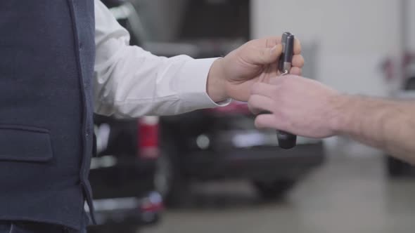 Close-up of Male Caucasian Hands Giving Car Keys To Unrecognizable Worker. Owner Giving His