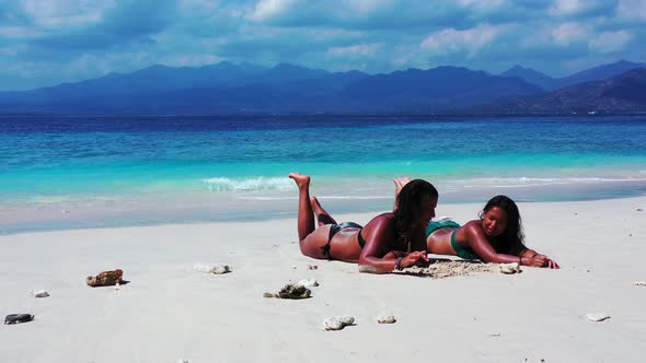 Pretty happy ladies on photoshoot by the sea on beach on sunny blue and white sand background 4K