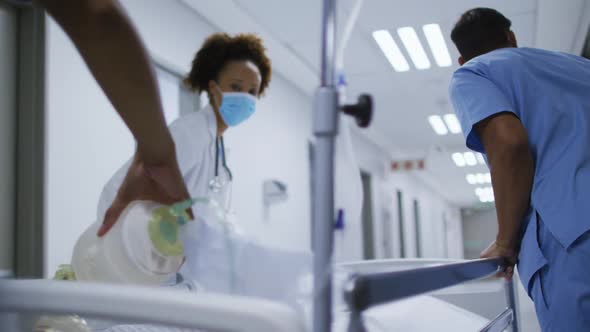 Diverse female and male doctors wearing face mask transporting patient