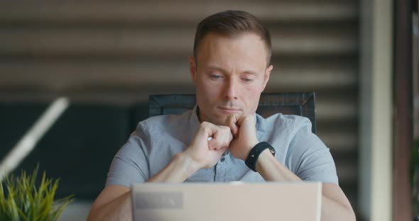 Focused Young Man is Sitting in Room at Laptop