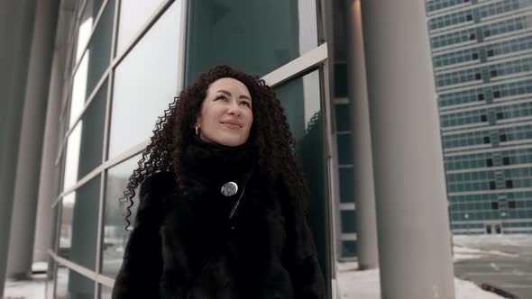 a Curlyhaired Stylish Middleaged Brunette Woman in a Black Fur Coat Walking Alone in the City on a