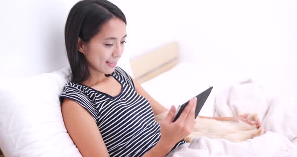 Woman watching on tablet and lying on bed with her dog