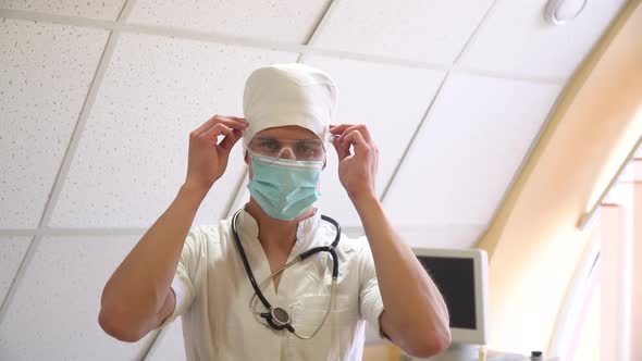 Young Doctor in Medical Mask Puts on Glasses in Hospital