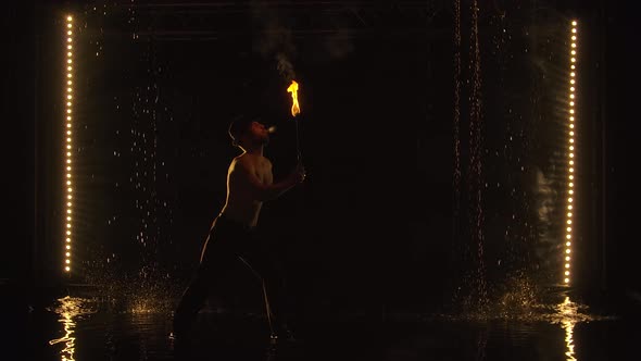 The Fakir Breathes Fire in a Dark Studio in the Rain. A Silhouette of a Half Naked Man