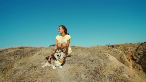 Beautiful Happy and Affectionate Laughing Girl in Yellow Dress with Cute Pet Corgi Dog Sitting on