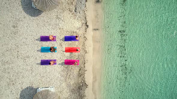 Aerial view of group of people doing yoga on colourful mats on the beach.