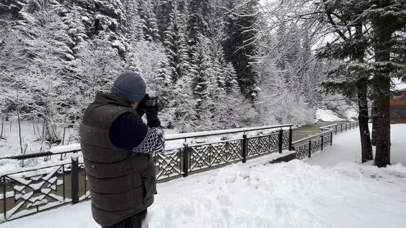 Man Photographer Shoots Snowcovered Trees and a Mountain River