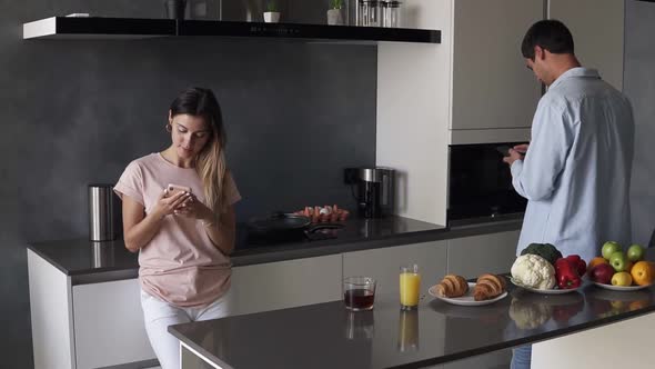 Young Couple Looking at Something on Their Smartphones Screen in the Kitchen with Modern Loft Design