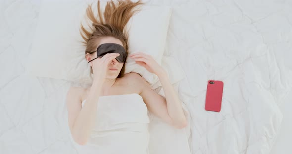 Young Woman Turns Off the Alarm on Her Cell Phone While Waking Up in the Morning
