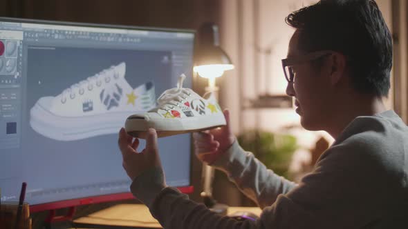 Asian Male Footwear Designer Holding And Looking At The Colourful Pattern Sneakers While Designing 