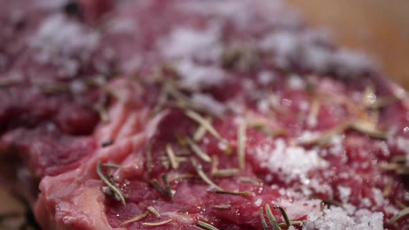Salt Falling on Raw beef Steak with rosemary on board