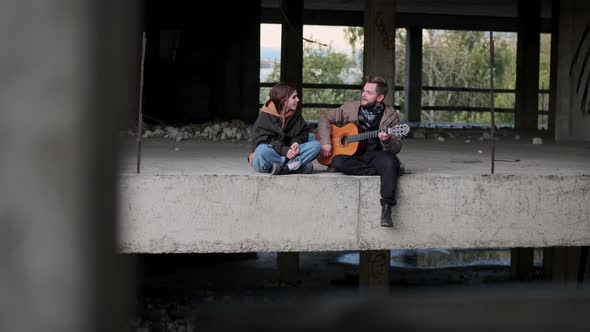 Guy with Guitar and Woman Sit on Floor in Abandoned Building Near to Each Other