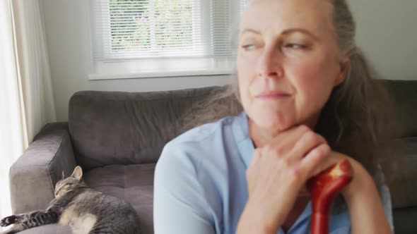 Senior caucasian woman wearing blue shirt and sitting with cat in living room