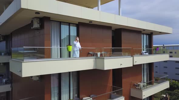 Drone view of woman in white coat with cup of coffee, on hotel balcony