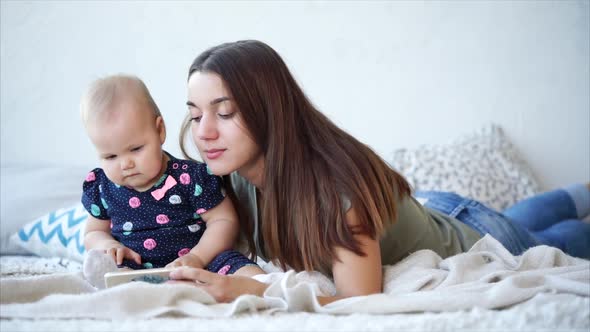 Attractive Woman and Her Cute Baby Lie in Bed and Watch Cartoons on Mobile Phone