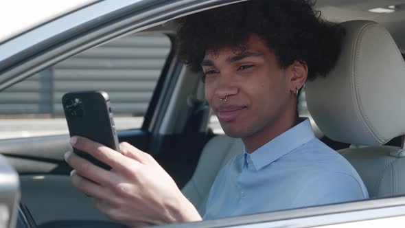 Afroamerican Student is Using Smartphone Sitting in Car Communicating in Social Nets Male User of