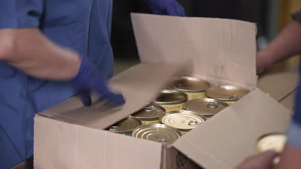 Female Hands in Blue Protective Gloves Packs Cans of Meat in Boxes at Factory