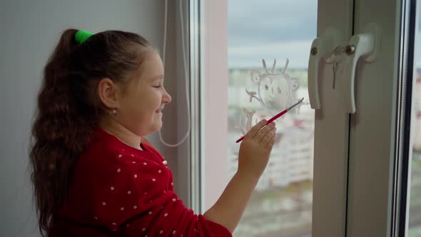 Child draw santa's gnome on window with white paints close-up. Caucasian female person decorate room