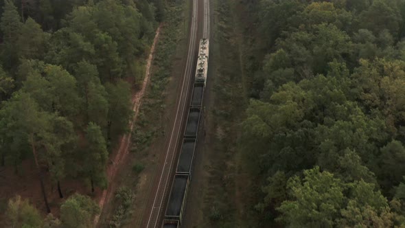 Freight train goes through the forest from aerial view.