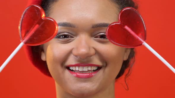 Happy Female Teenager in Stylish Red Beret Holding Heart Candy Front of Eyes