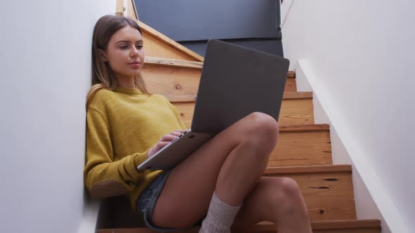 Woman using laptop while sitting on stairs at home