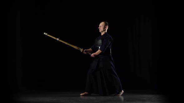 Masculine Kendo Warrior Practicing Martial Art with the Bamboo Bokken on Black Background.