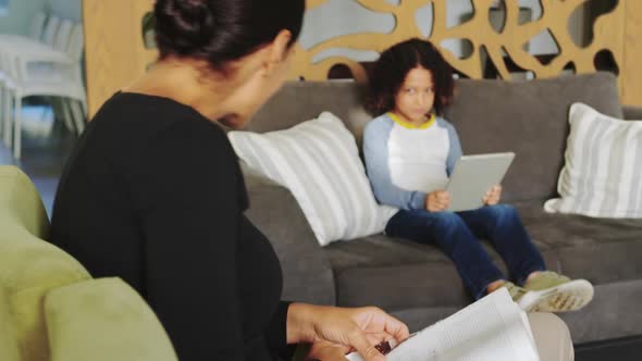 Side view of Caucasian woman reading magazine and African american boy using digital tablet on sofa